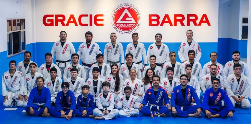 Alunos Kids, Teens e Adultos juntos em frente ao painel da Gracie Barra